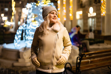 Girl walking in Christmas market decorated with holiday lights in the evening. Feeling happy in big city. Spending winter vacations