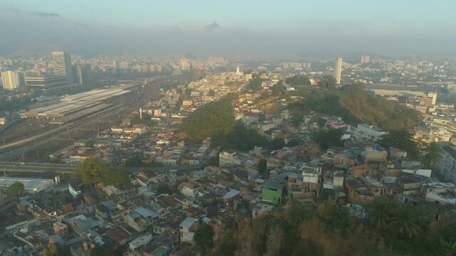 Early morning sideways tracking aerial of downtown central Rio de Janeiro, Brazil with wide view of favelas, transport links and misty mountains in the background