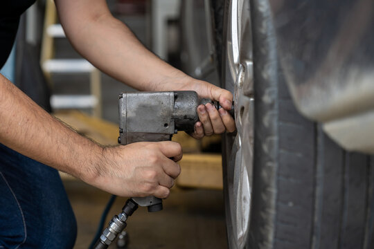 Hands of mechanic using pneumatic wrench changing tyre of car at auto repair shop. Male mechanic changing, repair and maintenance wheel on car with electric drill to loosen the bolts