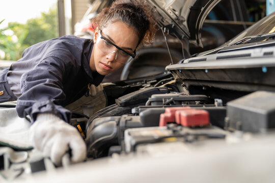 Female mechanic working at the garage. Professional female car mechanic examining, repair and maintenance under hood of car at auto car repair service. Car service and Maintenance concept - Powered by Adobe