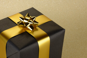 Caja de regalo negra y dorado sobre fondo de brillantina dorada en forma de cubo