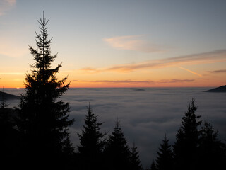 Fototapeta premium View from mountain range to the valley above fog and clouds at sunset