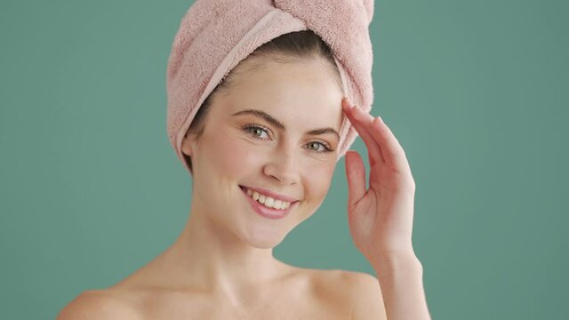 A smiling woman with a towel on her head is posing standing isolated over blue background in studio