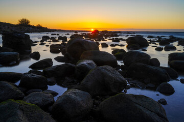 Boulders laying in shallow water with an cold winter sunset in the background, at the island of Gotland in Sweden