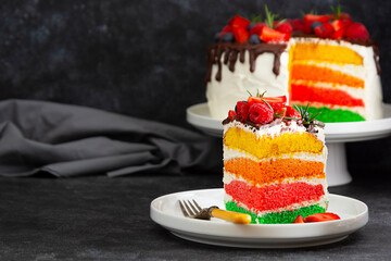 Rainbow slice of cake with fresh berries on dark background.