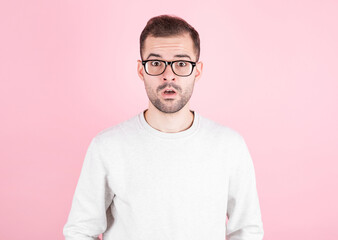 Surprised man in eyeglasses wearing white sweater over pink background