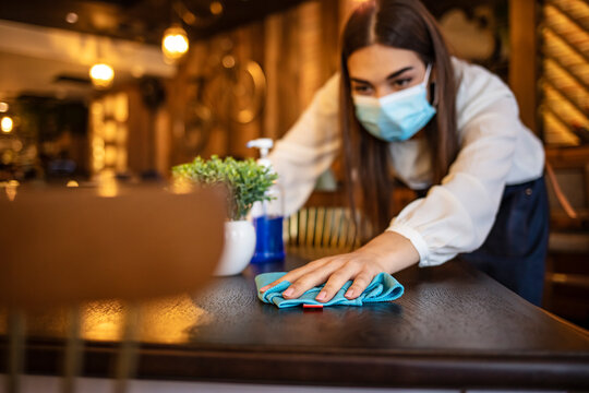 New Normal Startup Small Business Portrait Of  Woman Barista Wearing Protection Mask Cleaning Table In Coffee Shop While Social Distancing. New Normal Hygiene Restaurant Concept.