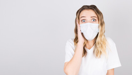Portrait of a young surprised woman in a medical mask isolated over grey background. Young girl patient stands against the wall background wirh fear in her eyes, copy space for text