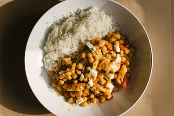 top view of chickpeas curry dish on wood table with natural light and basmati rice. Healthy organic vegetarian food with cheese
