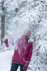 pretty ageless senior woman in winter forest, standing under falling snow. Carefree woman enjoying snow and winter time. She playing with snow. Winter leisure concept