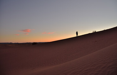 Eine Silhouette einer Person auf einer Sanddüne in der Wüste im Abendlicht