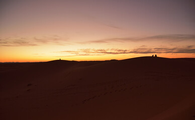 Fototapeta na wymiar Dämmerung in der Sahara mit Menschen, die auf Sandbergen sitzen und das Naturschauspiel beobachten