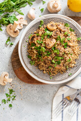 Quinoa stewed with mushrooms, onions, garlic, and parsley in a plate on a gray concrete background top view. Delicious and healthy vegetarian food. Quinoa with champignons.