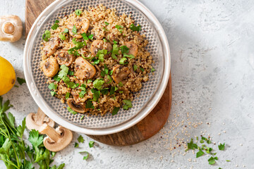 Quinoa stewed with mushrooms, onions, garlic, and parsley in a plate on a gray concrete background top view. Delicious and healthy vegetarian food. Quinoa with champignons.