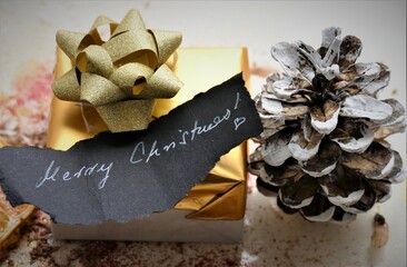 merry Christmas note with golden gift and pine cone winter background