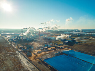 Factories, pipes with smoke on a Sunny snowless winter day, photo from a drone. Concept of ecology and nature protection