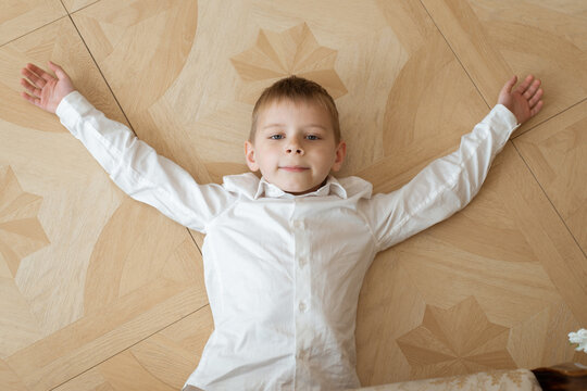 A young boy is lying on the floor. In a white shirt and black pants.