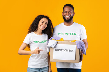 Two Cheerful Volunteers Holding Donation Box On Yellow Studio Background
