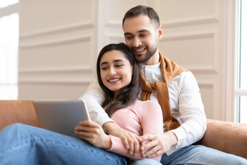 Happy Modern Arab Couple Using Digital Tablet Sitting At Home