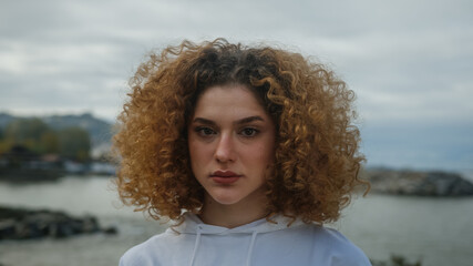 Portrait of young woman in white sportswear with curly hair behind sea landscape.