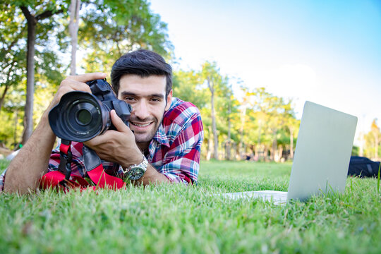 portrait of young business handsome man using dslr digital camera and take a photo with natural at public park. He has a bright smile and happiness. Ideas for work outside and relaxing in the garden