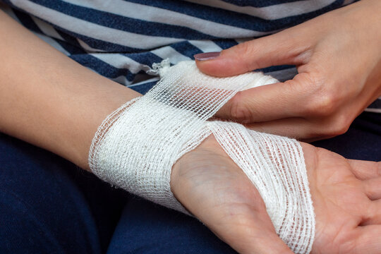Young woman bandaging her wrist. Wound care bandage, control bleeding. Bandaging a wrist wound with a gauze bandage. Close-up, warm tinting.