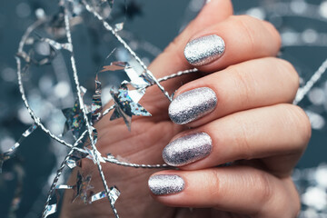 Female hand with beautiful holiday manicure - silver glittered nails with Christmas twisted wire...