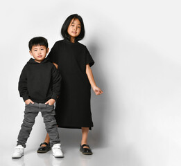 stylish brother and sister asian children posing in front of the camera in the studio on a white background. Cool boy in black hoodie and jeans with older sister in black dress having fun.