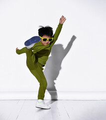 Fashion portrait of cute little kid boy in stylish green tracksuit dancing break against white studio wall. The concept of sports and healthy activities for the modern child.