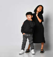 Portrait of two beautiful Asian children posing in front of the camera in the studio against a white background. A cool boy in a black hoodie and jeans with an older sister in a black dress is fun.