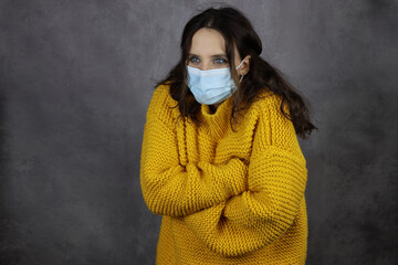 a young attractive girl froze in a medical mask in a yellow sweater on a gray space background