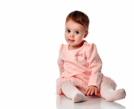Cute baby girl sits on a white background. Adorable little kid looking at the camera. The studio shot a portrait of a sweet baby wearing a pink skirt, sweater and tights.