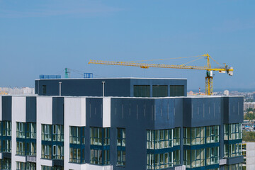 Top floor of  skyscraper. Construction site with yellow crane and building. Crane and building construction site against blue sky and city districts in the background.