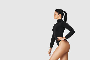 portrait of beautiful slim tanned woman with perfect body in black bodysuit posing on studio background. copy space