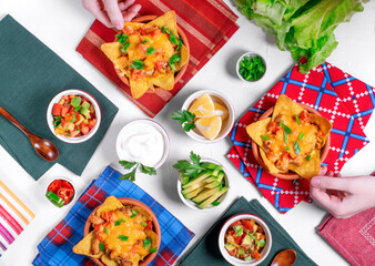 Nachos with chicken, mushroom and melted cheese served with assorted toppings on white table. Salsa, avocado, sour cream, lemons, green onion. Top view. Mexican food. Table setting