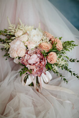 Wedding. The girl in a white dress and a guy in a suit sitting on a wooden chair, and are holding a beautiful bouquet of white, blue, pink flowers and greenery, decorated with silk ribbon