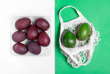 Green avocado in eco-friendly mesh bag and purple avocado in plastic package against the green and white geometric background. Choosing sustainability