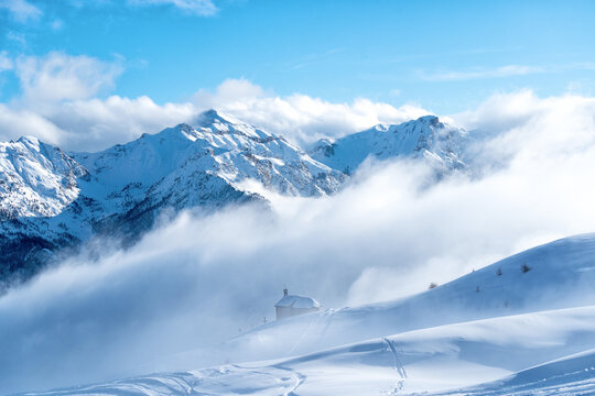 Snow covered mountain peaks above the clouds. High mountains in winter landscape. Briancon one of largest ski resort in Europe. View of the ski area and house with nobody around. New normal concept