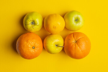 Ripe fruits: apples, lemon, oranges on a yellow background.