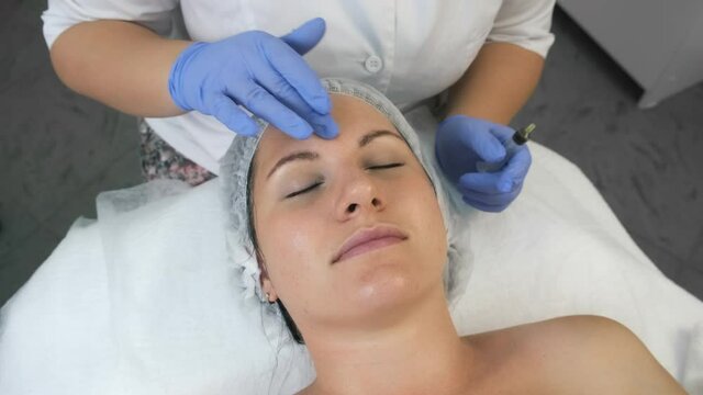 Cosmetologist is applying yellow peeling on woman's face massaging movements in beauty clinic. Beautician is making cure procedure on patient's face, closeup top view.