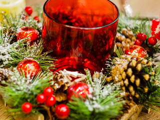 New Year's red candlestick in a handmade wreath, decorated with toys, ribbons, pine cones and a Christmas tree.