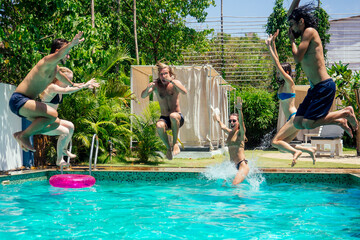 Group of happy six friends drinking jumping in pool day party with splash