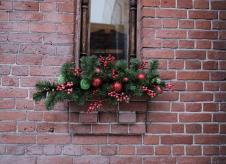 Fototapeta na wymiar Window in an old brick building. Decoration for Christmas and New Year. Green branches, red balls.