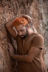 Portrait of young sad man with orange hair leaning on a stone wall
