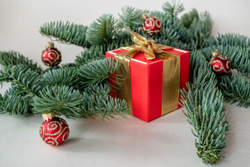 Fototapeta na wymiar Red Christmas gift box with golden ribbon decorated with green fir branches and red ornaments