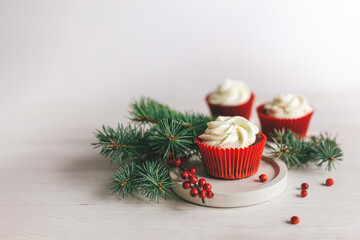 Tasty cupcakes decorated with spruce branches and red berries on a white wooden background. Sweets for the celebration Christmas.