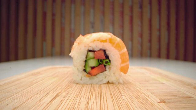 Hand takes away pieces of sushi roll with chopsticks from wooden board