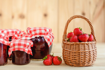 Strawberry jam in a jar on a wooden background with fresh strawberries in a basket.