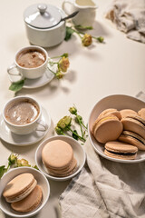 Frothy coffee in white cups, delicious French macaroons. Dessert still life on a beige background. Vertical shot