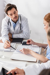 Doctor pointing at papers near digital tablet and nurse on blurred foreground